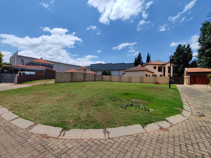 A vacant residential plot featuring a well-maintained lawn, perimeter walling, and paved access, situated within a developed residential estate.