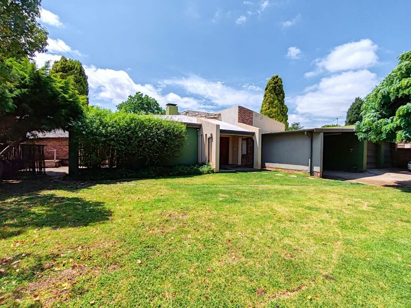 Front view of a residential house featuring a lawn, attached carport, and brick architectural details under a clear sky.