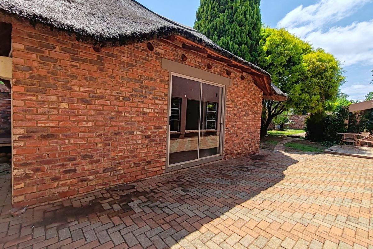Rear exterior view featuring a traditional thatched roof, exposed brick walls, and a paved patio area with sliding door access.