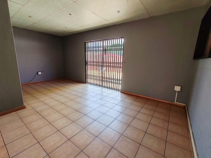 An empty living room featuring ceramic floor tiles, recessed lighting, and a sliding glass door with a fitted metal security gate.