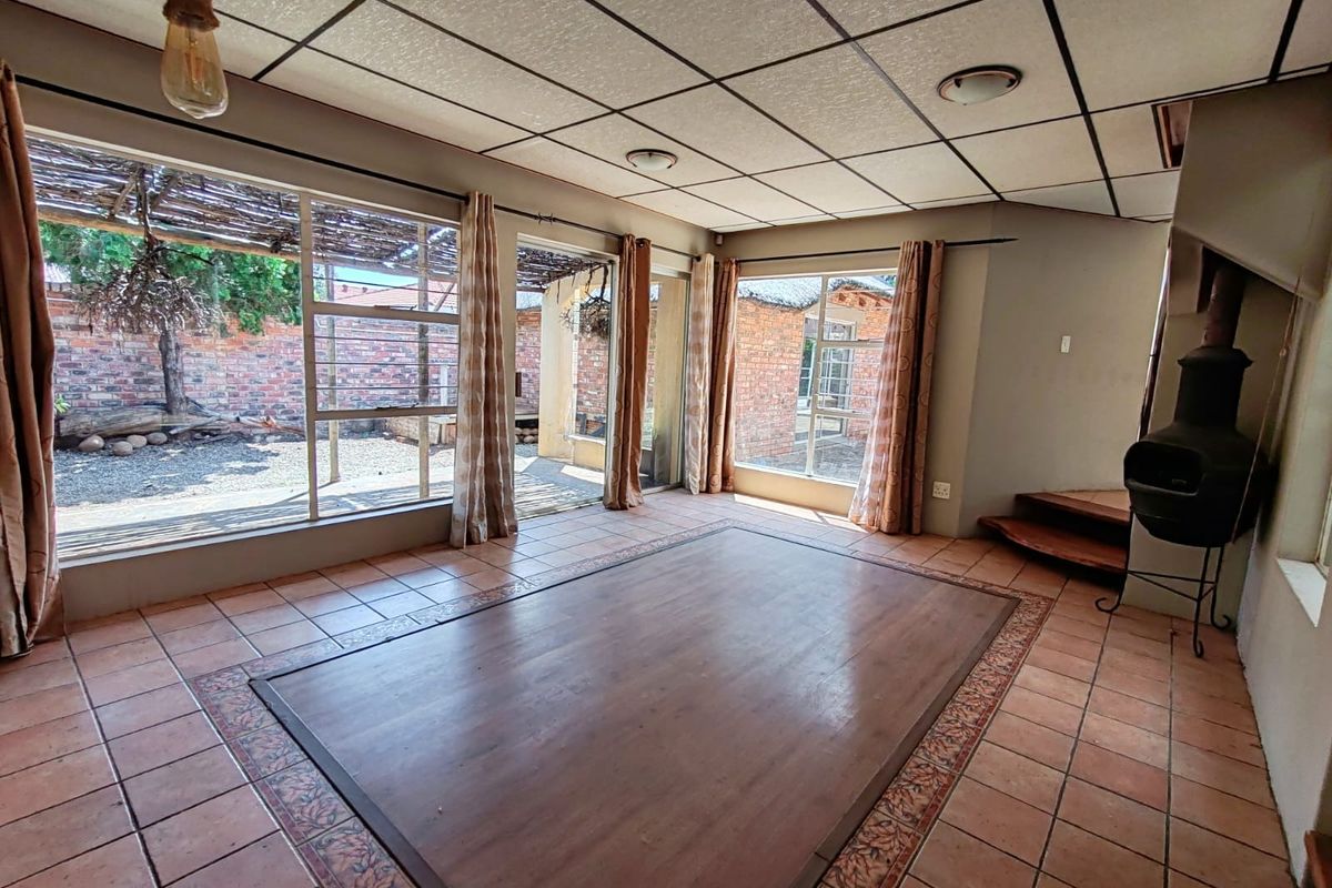Spacious living area featuring tiled floors with a wooden inlay, a freestanding fireplace, and large glass doors providing access to the rear garden.