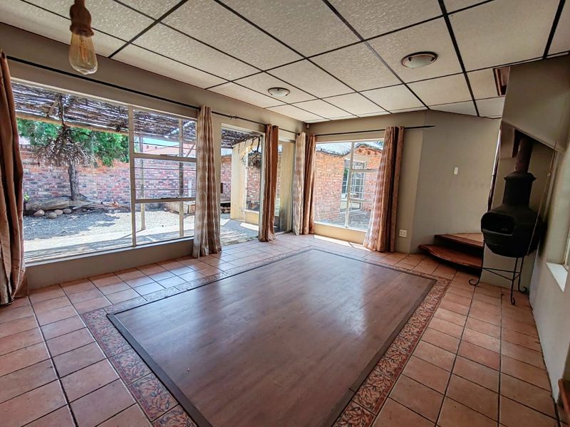 Spacious living area featuring tiled floors with a wooden inlay, a freestanding fireplace, and large glass doors providing access to the rear garden.