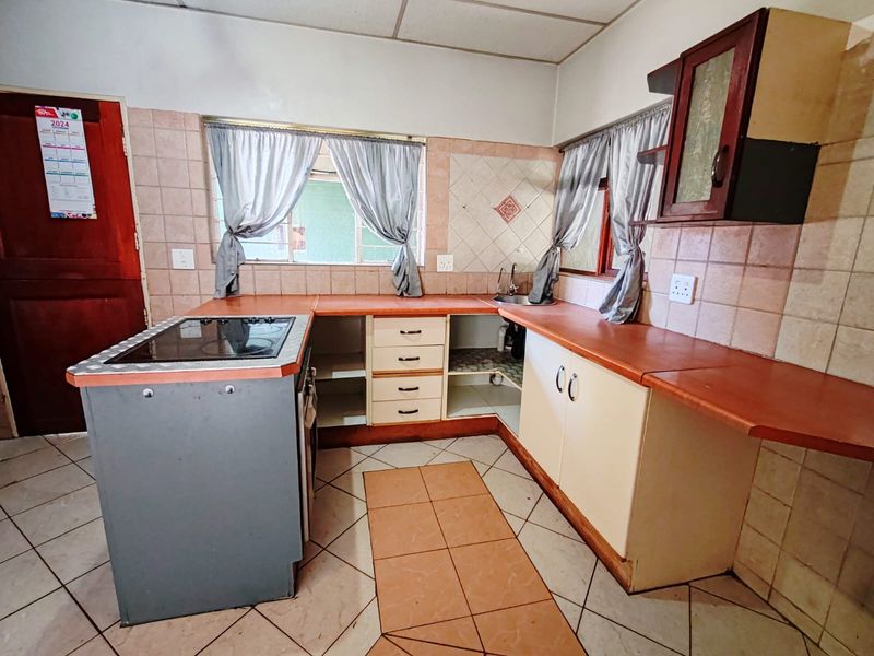 A functional kitchen featuring built-in cabinetry, laminate countertops, a ceramic tile backsplash, and a built-in electric hob, offering potential for modernization.