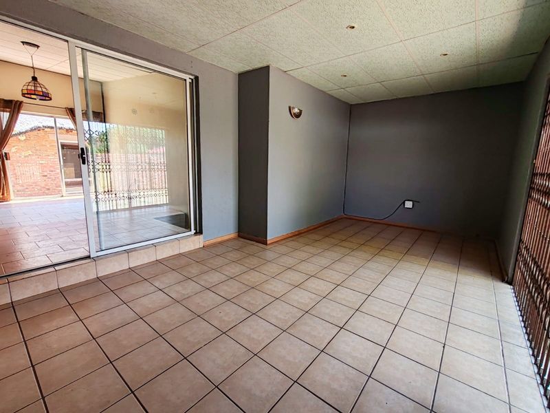 An empty, covered patio area featuring tiled flooring, recessed lighting, and a large sliding glass door leading to the exterior.