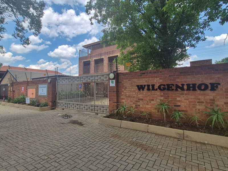Front entrance view of Wilgenhof apartment complex featuring a secure brick boundary wall, electric fencing, and a paved driveway entrance.