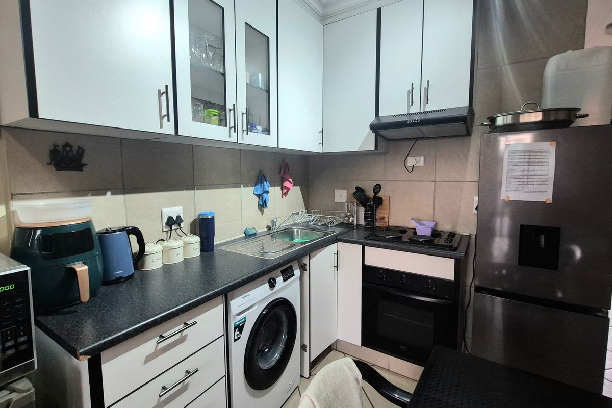 Compact kitchen featuring white cabinetry, dark laminate countertops, integrated oven and hob, and tiled finishes, providing a functional and efficient workspace.