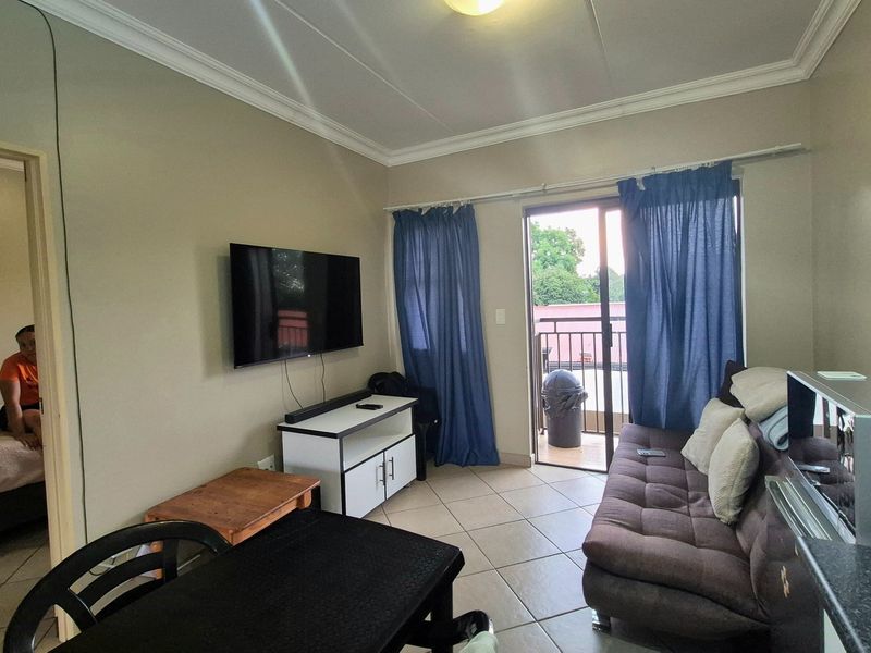 A living room featuring tiled flooring, cove cornicing, and a sliding glass door providing access to an outdoor balcony area.