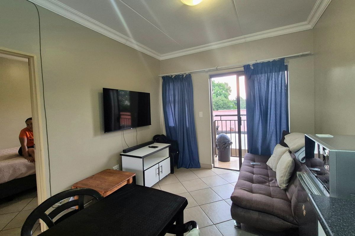 A living room featuring tiled flooring, cove cornicing, and a sliding glass door providing access to an outdoor balcony area.