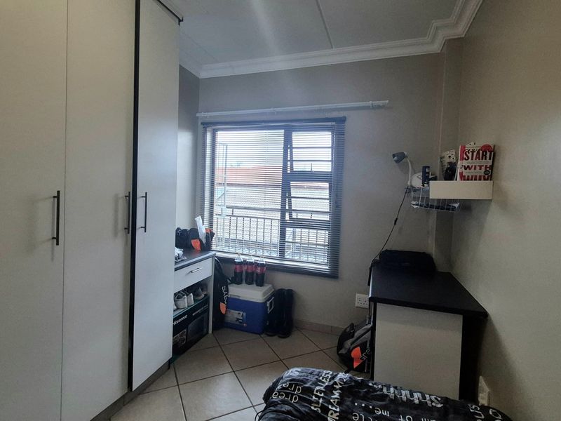A functional bedroom featuring built-in cupboards, tiled flooring, and a window with fitted blinds, offering a practical living space.