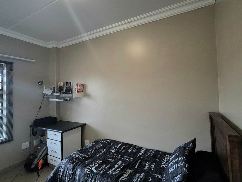 A bedroom featuring neutral wall paint, crown molding, and a window with fitted blinds.
