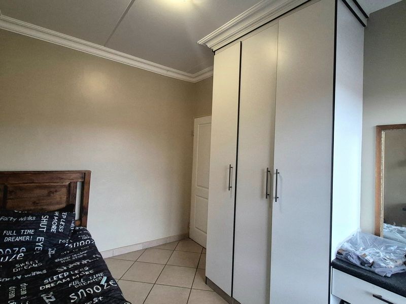 A bedroom featuring tiled flooring, crown molding, and a large built-in wardrobe providing ample storage space.