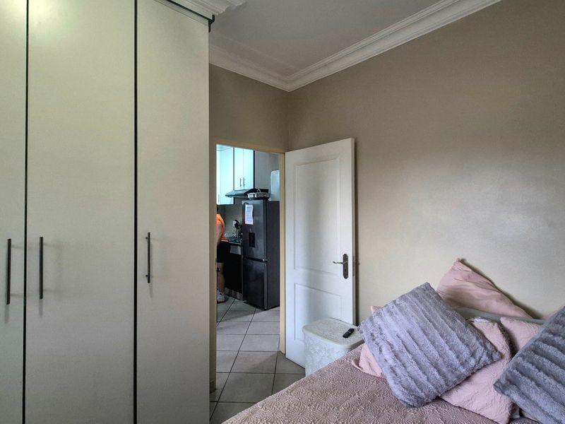 Bedroom featuring built-in cupboards, crown molding, and tiled flooring, with a view through to the adjacent kitchen area.