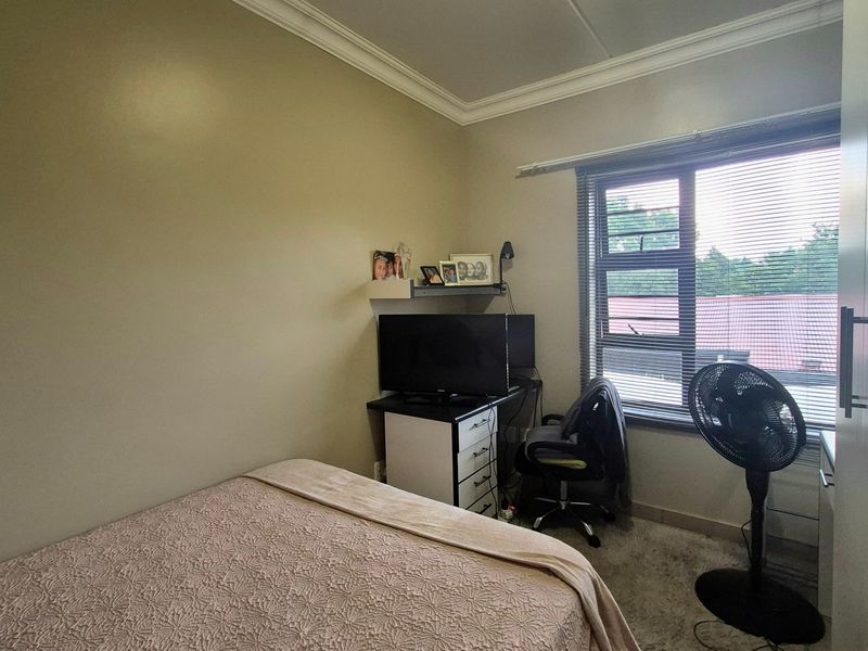 A functional bedroom featuring a built-in wardrobe, neutral wall finishes, and a window with fitted venetian blinds.