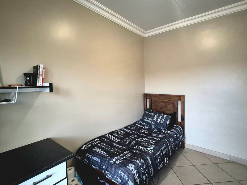 A compact bedroom featuring neutral wall tones, crown molding, and tiled flooring, providing a functional space for rest.