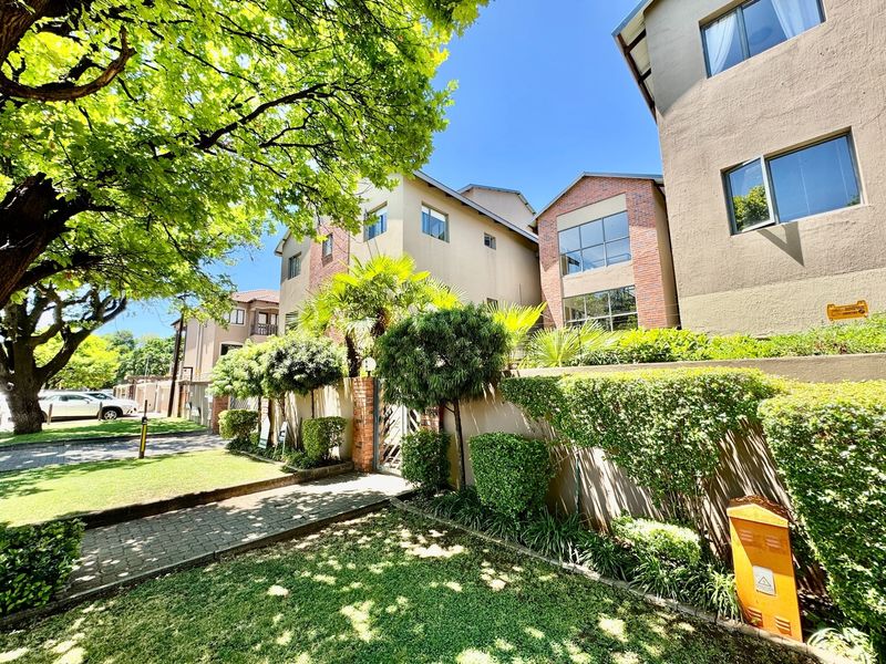 Exterior view of the apartment complex featuring a well-maintained garden, paved walkway, and brick and plaster facade with aluminum window frames.