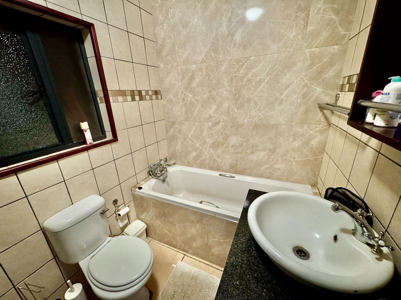 A functional bathroom featuring a bathtub, toilet, and a vessel sink set into a granite vanity countertop with neutral wall tiling.