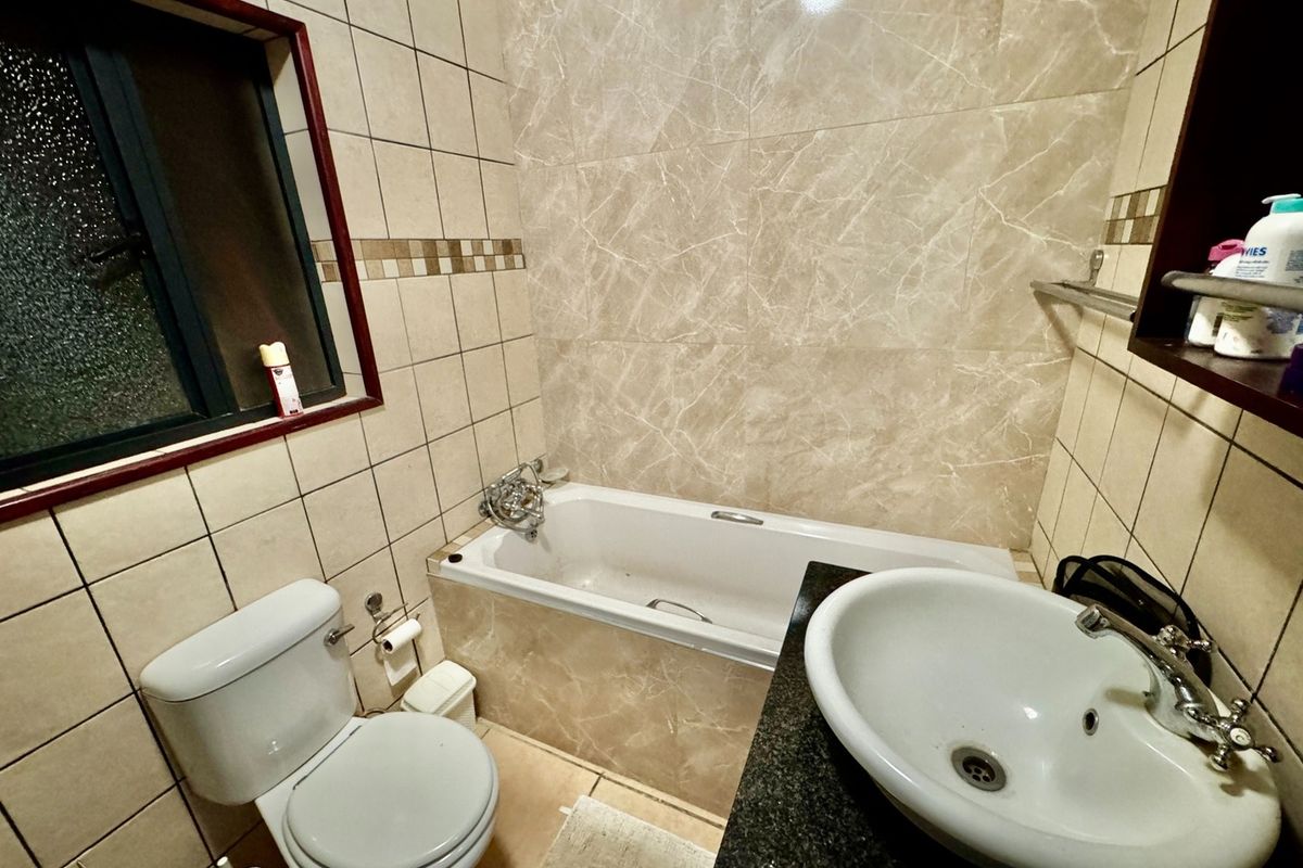 A functional bathroom featuring a bathtub, toilet, and a vessel sink set into a granite vanity countertop with neutral wall tiling.