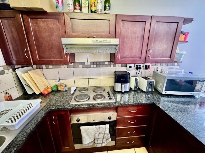 A functional kitchen featuring dark wood cabinetry, granite countertops, a built-in oven, electric hob, and a tiled backsplash.