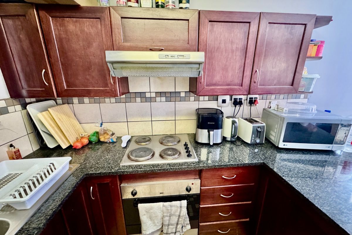 A functional kitchen featuring dark wood cabinetry, granite countertops, a built-in oven, electric hob, and a tiled backsplash.