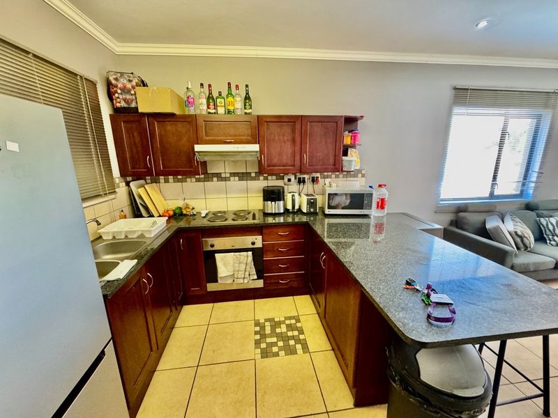 Open-plan kitchen featuring dark wood cabinetry, granite countertops, built-in oven, electric hob, and a breakfast bar, seamlessly connected to the living area.