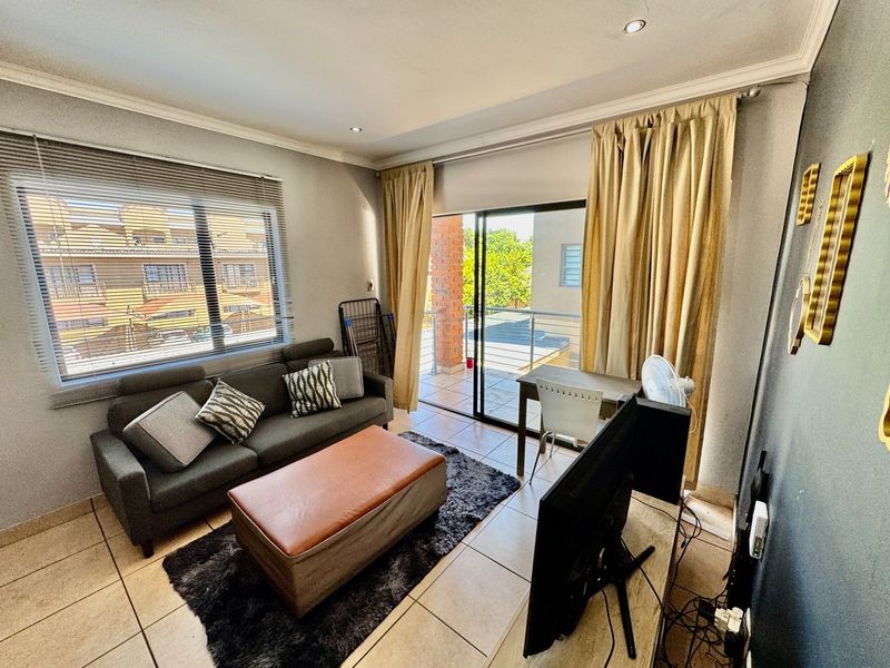 A functional living room featuring tiled flooring, recessed lighting, and a sliding glass door providing direct access to an outdoor balcony area.