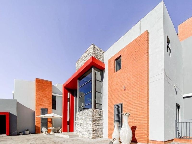 Modern architectural home exterior featuring a striking combination of red brick, stone cladding, and large glass windows with an integrated garage.