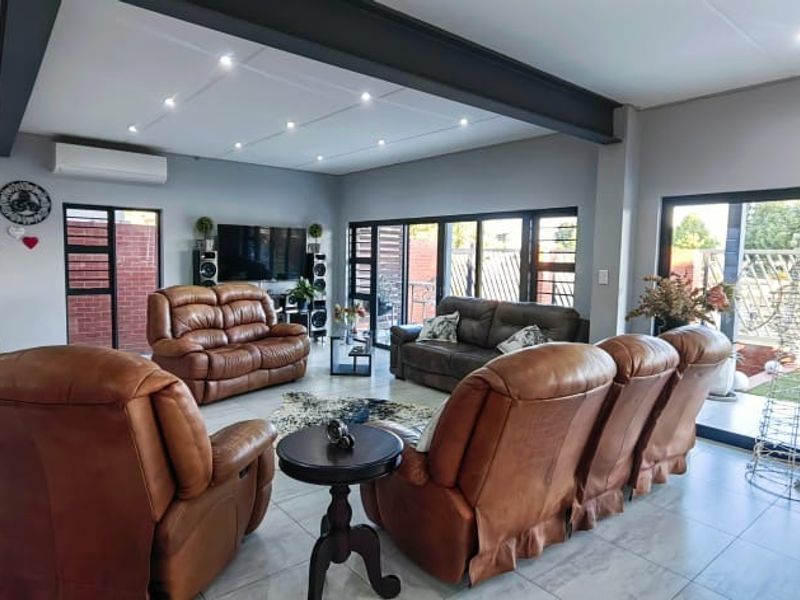 Spacious open-plan living and dining area featuring modern tiled floors, exposed steel beams, recessed lighting, and large sliding doors leading to the outdoor patio.