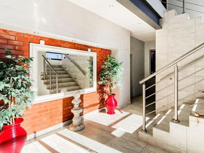 Spacious entrance hall featuring a striking exposed brick feature wall, modern tiled flooring, and a contemporary staircase with stainless steel railings.