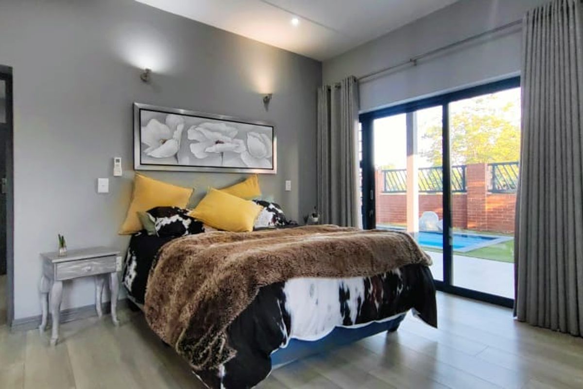 A well-maintained bedroom featuring modern laminate flooring, wall-mounted lighting, and large sliding glass doors providing direct access to the outdoor pool area.