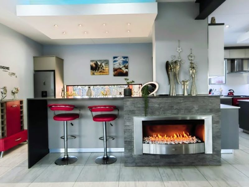 Spacious open-plan living and kitchen area featuring a modern built-in fireplace with stone cladding, recessed ceiling lights, and contemporary kitchen cabinetry.
