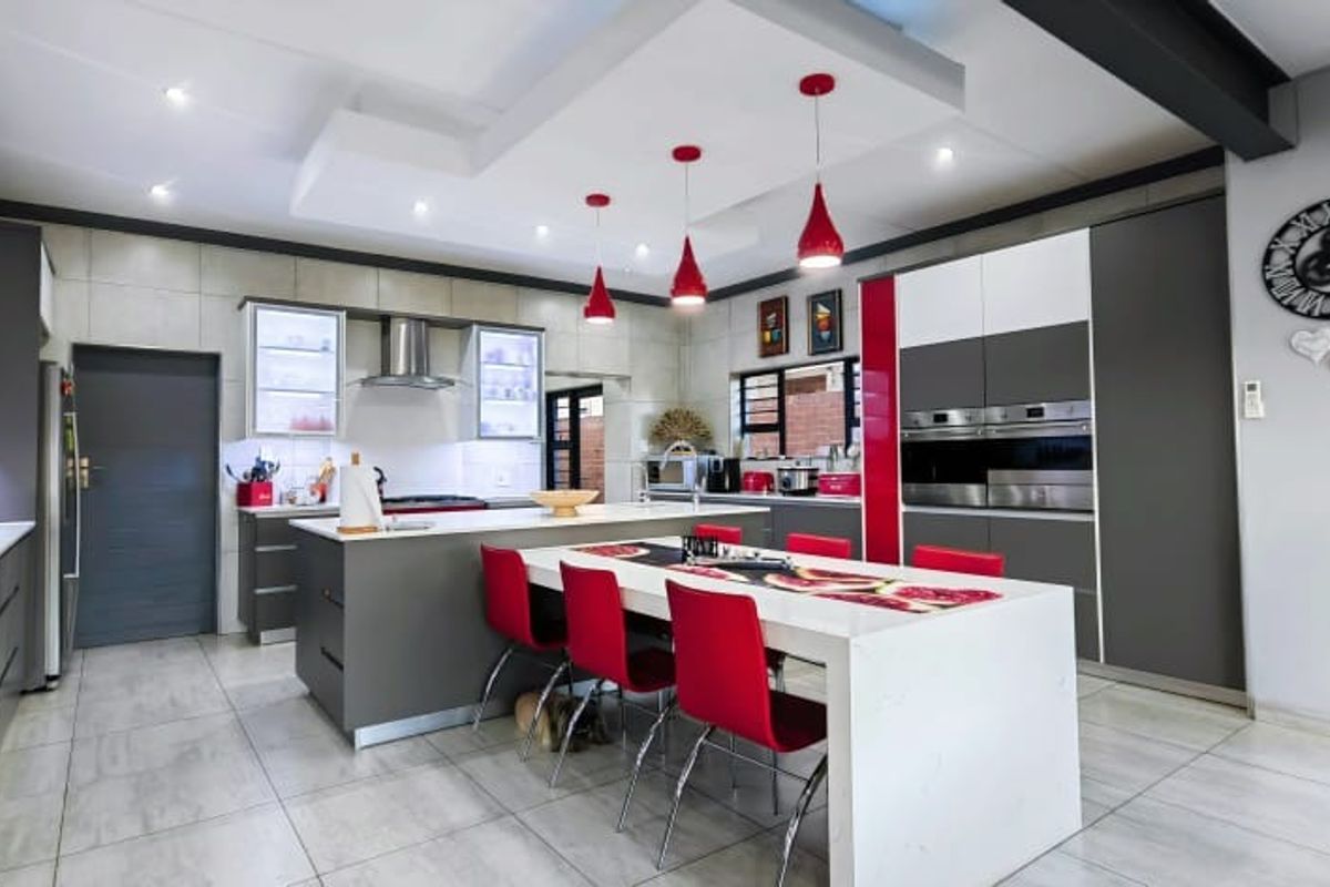 Modern kitchen featuring a large central island, integrated appliances, sleek cabinetry, and a contemporary drop ceiling with pendant lighting.