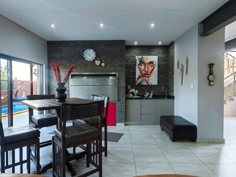 Modern open-plan entertainment area featuring a built-in braai, stone-clad feature wall, tiled floors, and seamless access to the outdoor pool area.