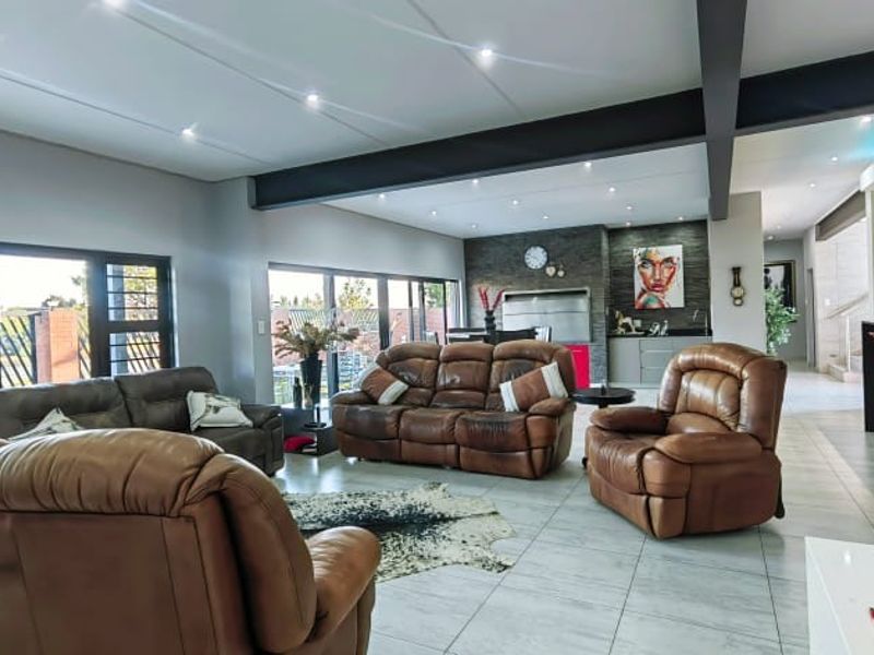 Spacious open-plan living area featuring modern tiled floors, recessed lighting, an exposed structural beam, and a stone-clad fireplace, with large sliding doors to the exterior.