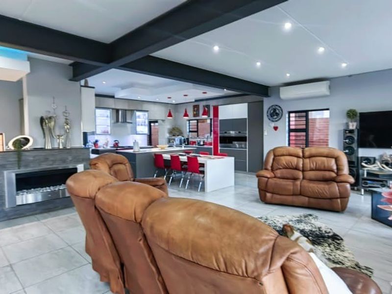 Spacious open-plan living area featuring a modern kitchen with island, built-in fireplace with stone cladding, exposed steel beams, and contemporary recessed lighting.