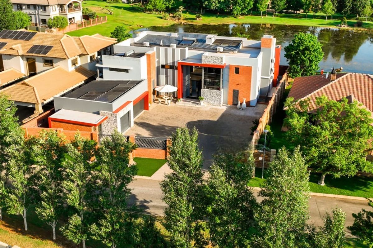 Aerial view of a modern contemporary residence featuring solar panels, a double garage, and a paved driveway, situated in a scenic estate setting.