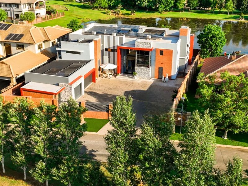 Aerial view of a modern contemporary residence featuring solar panels, a double garage, and a paved driveway, situated in a scenic estate setting.