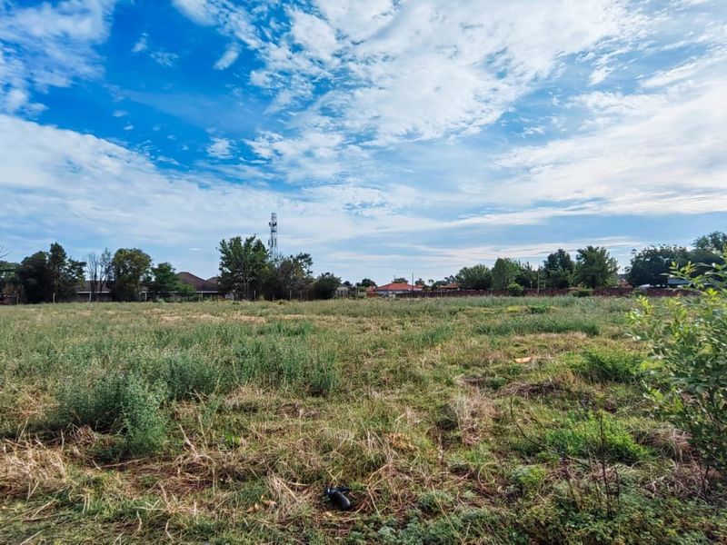 A wide-angle view of a vacant residential plot featuring open grassland and surrounding neighborhood trees.