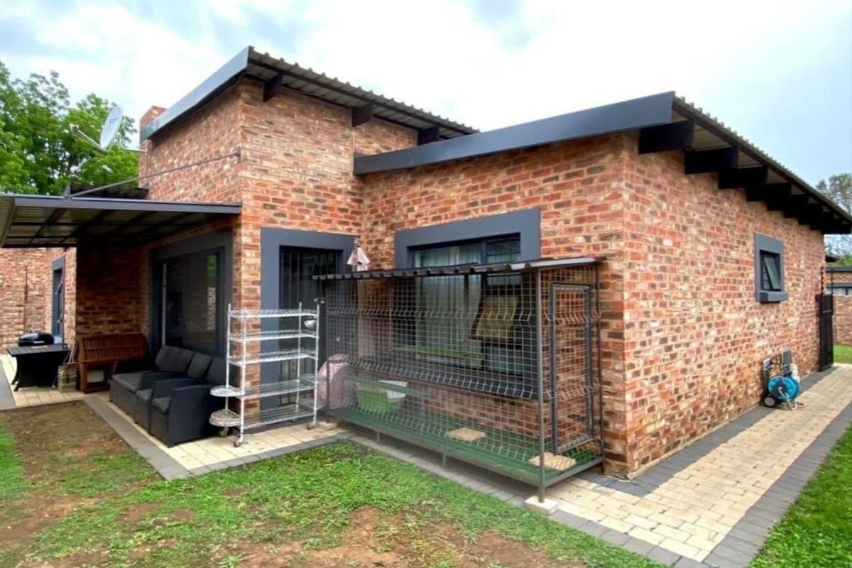 Rear view of a face brick house featuring a paved patio area, corrugated metal roofing, and modern dark-framed windows.