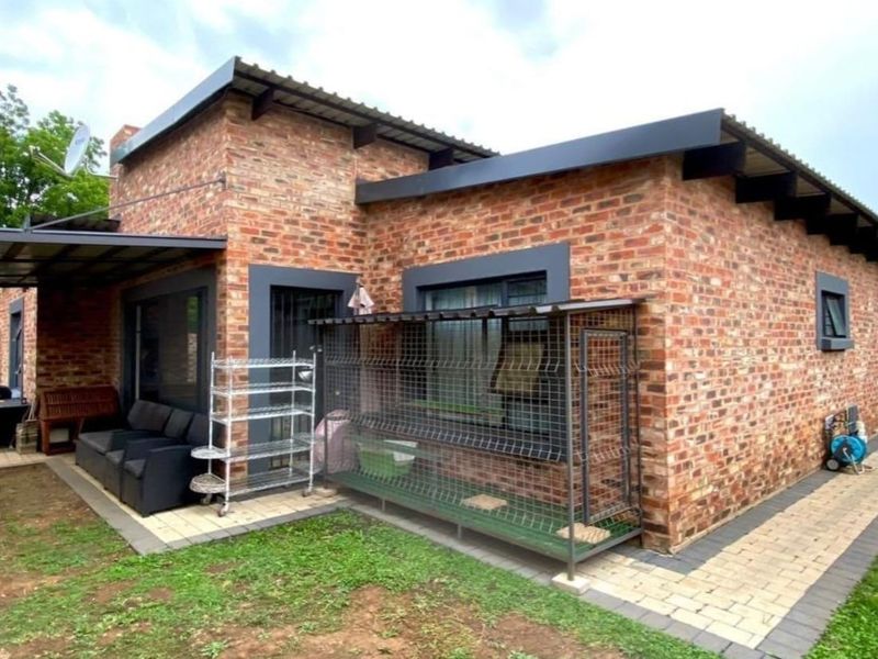 Rear view of a face brick house featuring a paved patio area, corrugated metal roofing, and modern dark-framed windows.