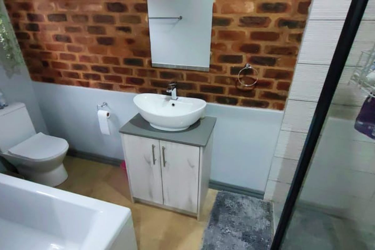 A modern bathroom featuring a vessel sink on a vanity cabinet, a bathtub, a separate shower enclosure, and a distinctive exposed brick feature wall.