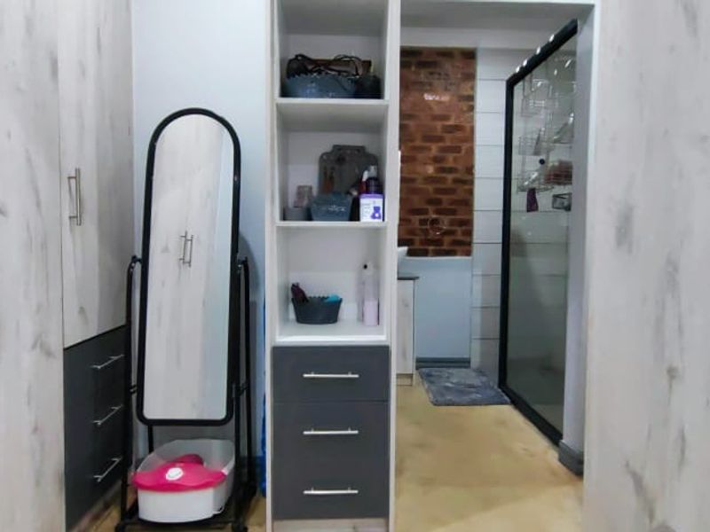 A bedroom dressing area featuring modern built-in cupboards with light wood-grain finish and a central open shelving unit with integrated drawers.
