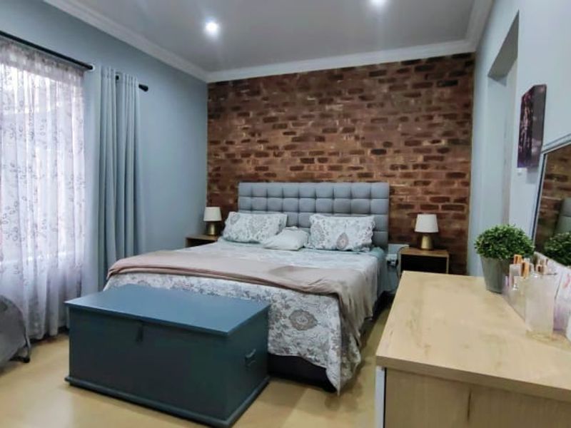 A well-maintained bedroom featuring an exposed brick accent wall, recessed downlighting, and neutral laminate flooring, creating a warm and inviting atmosphere.