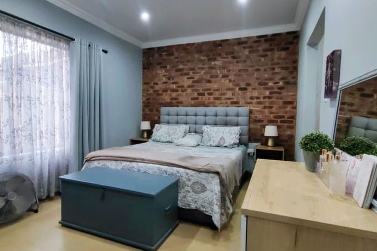 A well-maintained bedroom featuring an exposed brick accent wall, recessed downlighting, and neutral laminate flooring, creating a warm and inviting atmosphere.