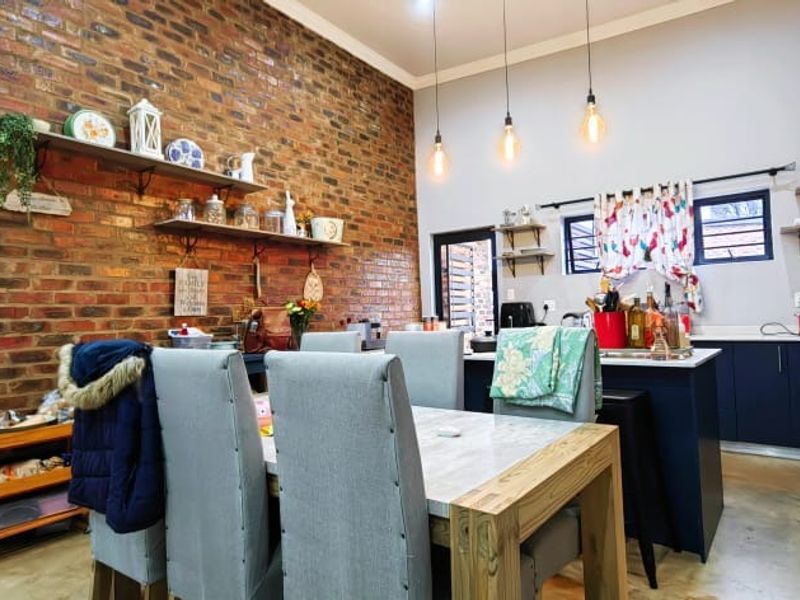 Spacious open-plan kitchen and dining area featuring a striking exposed brick feature wall, modern cabinetry, kitchen island, and polished concrete flooring.