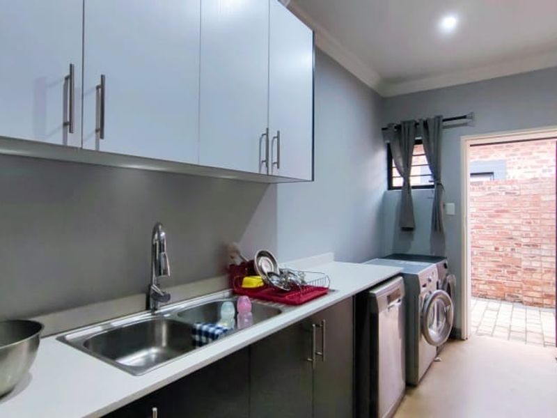 A functional scullery featuring modern built-in cabinetry, a double sink, and direct access to an outdoor area through a secure door.