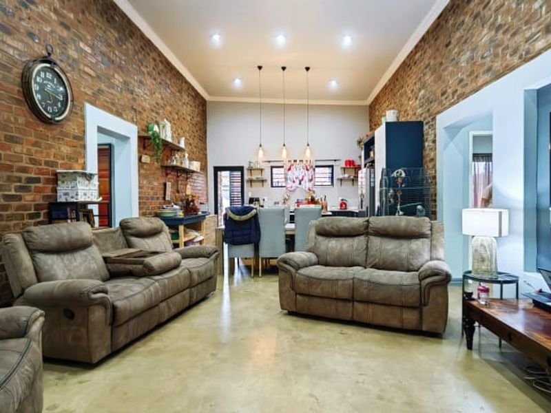 Spacious open-plan living and dining area featuring exposed brick walls, polished concrete floors, and modern recessed lighting with an integrated kitchen.
