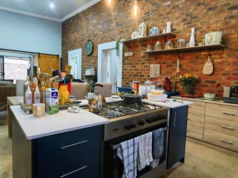 Spacious open-plan kitchen featuring an exposed brick feature wall, central island with gas hob, and modern cabinetry, seamlessly flowing into the living area.