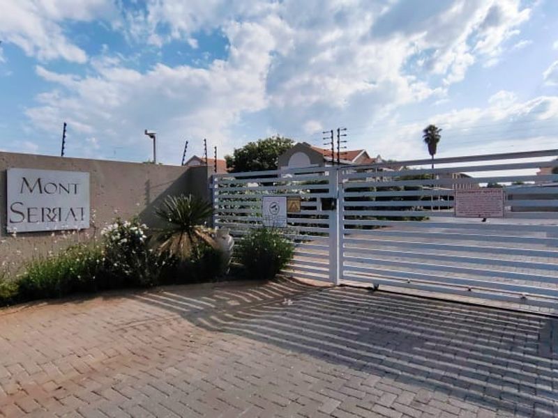 The main entrance to the Mont Serai complex, featuring a secure sliding gate, paved driveway, and perimeter boundary wall with electric fencing.