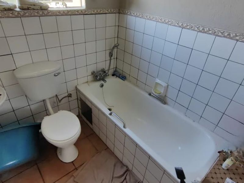 A dated bathroom featuring a bathtub, toilet, and pedestal basin with white wall tiling. The space requires maintenance and cosmetic updates to the wall finishes.