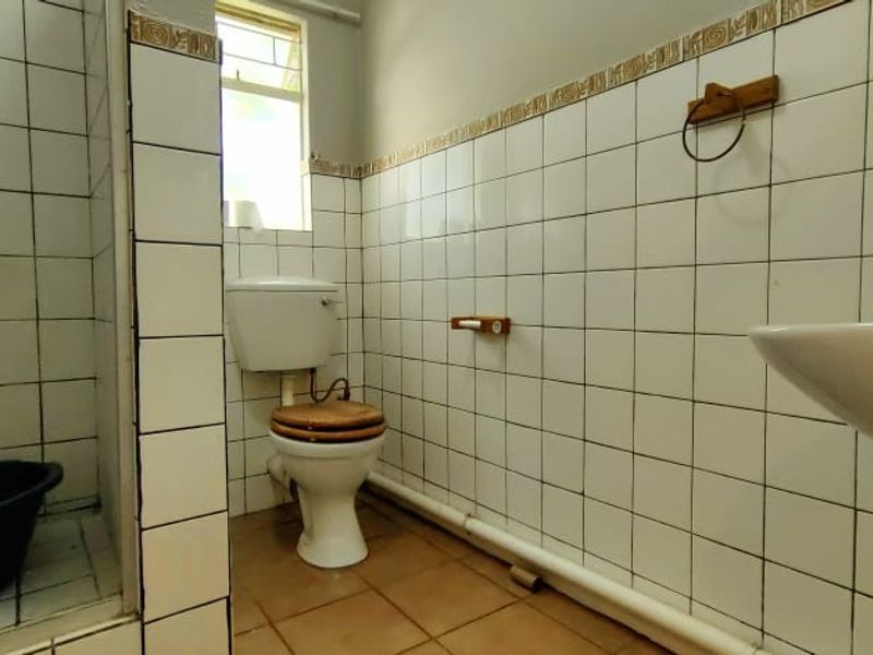 A dated bathroom featuring a shower enclosure, pedestal basin, and toilet with white wall tiling and exposed plumbing.